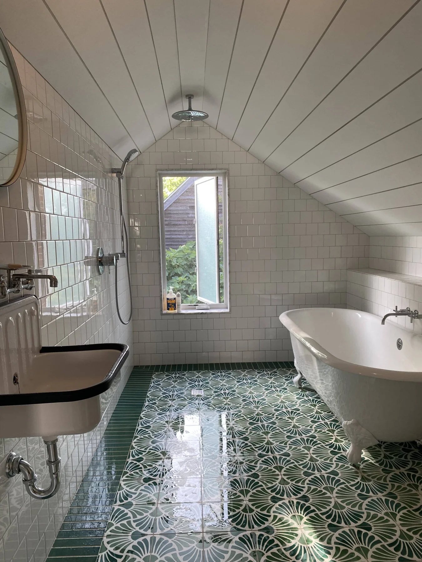 White subway tiles, flower themed tiled floor in several shades of green and white wood ceiling. A Victorian white clawfoot tub and sink along with a shower complete this simple bathroom.